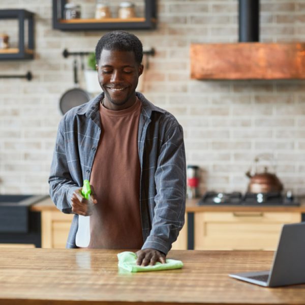 Portrait of smiling African-American man enjoying spring cleaning in modern home interior, copy space