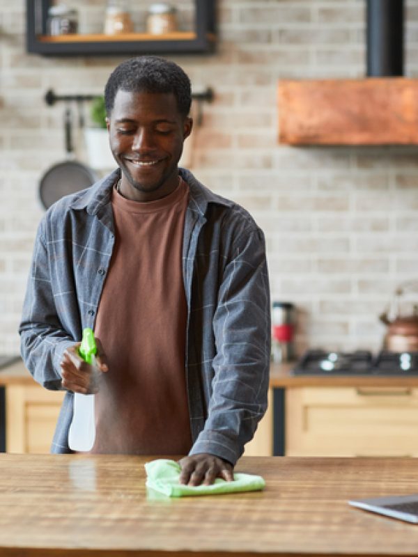 Portrait of smiling African-American man enjoying spring cleaning in modern home interior, copy space